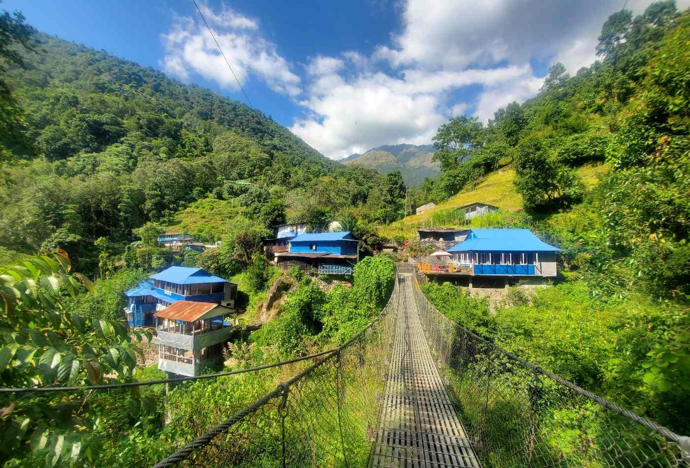 Suspension bridge with greeny sourrounding hills and blue roof houses in front. 