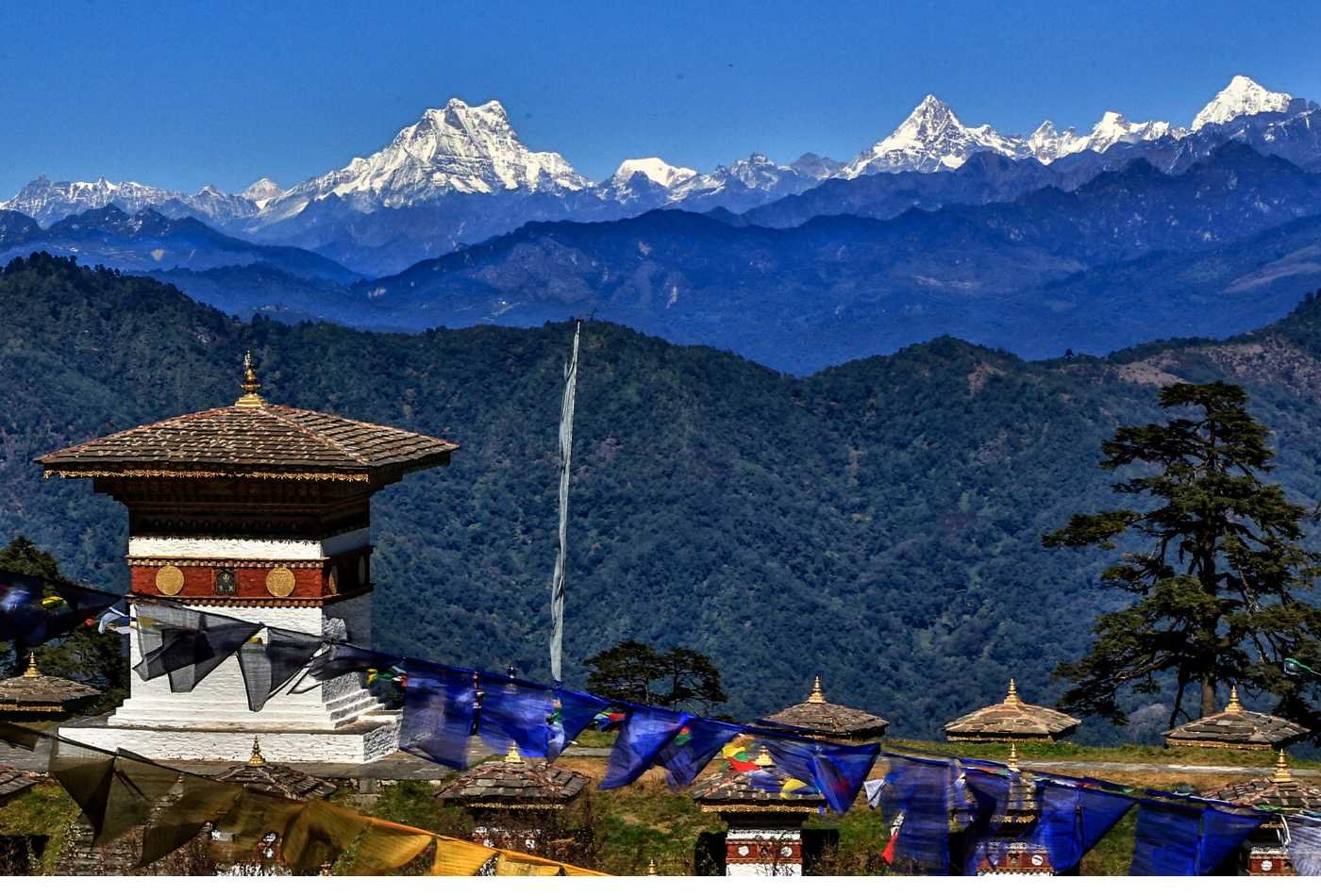 Dochu La Pass, a mountain pass in Bhutan, with a stunning view of snow-capped peaks in the background, and a small monuments in foreground.