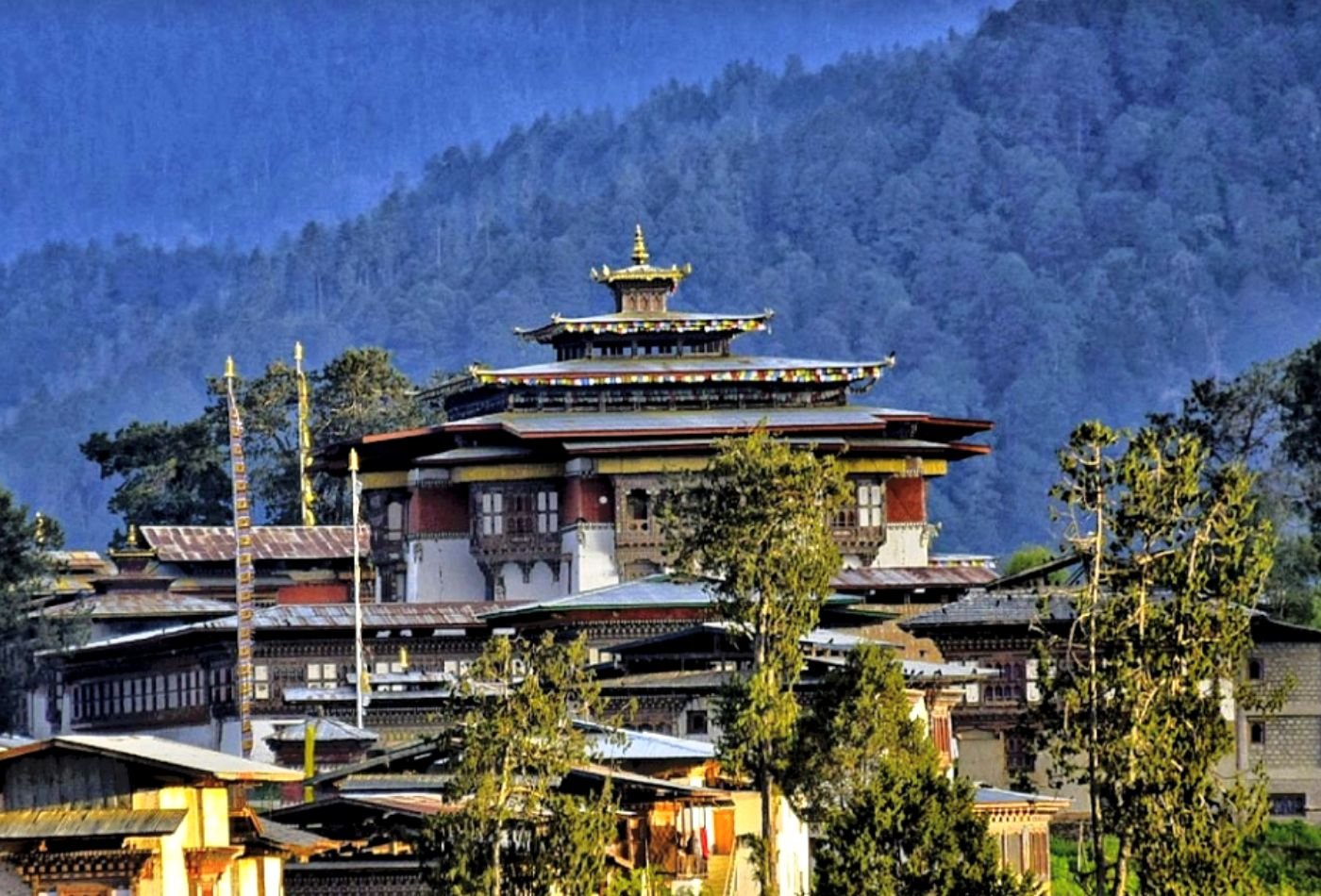 A picture of the Gangtey Monastery, featuring its red roof and the lush green forest in the background.