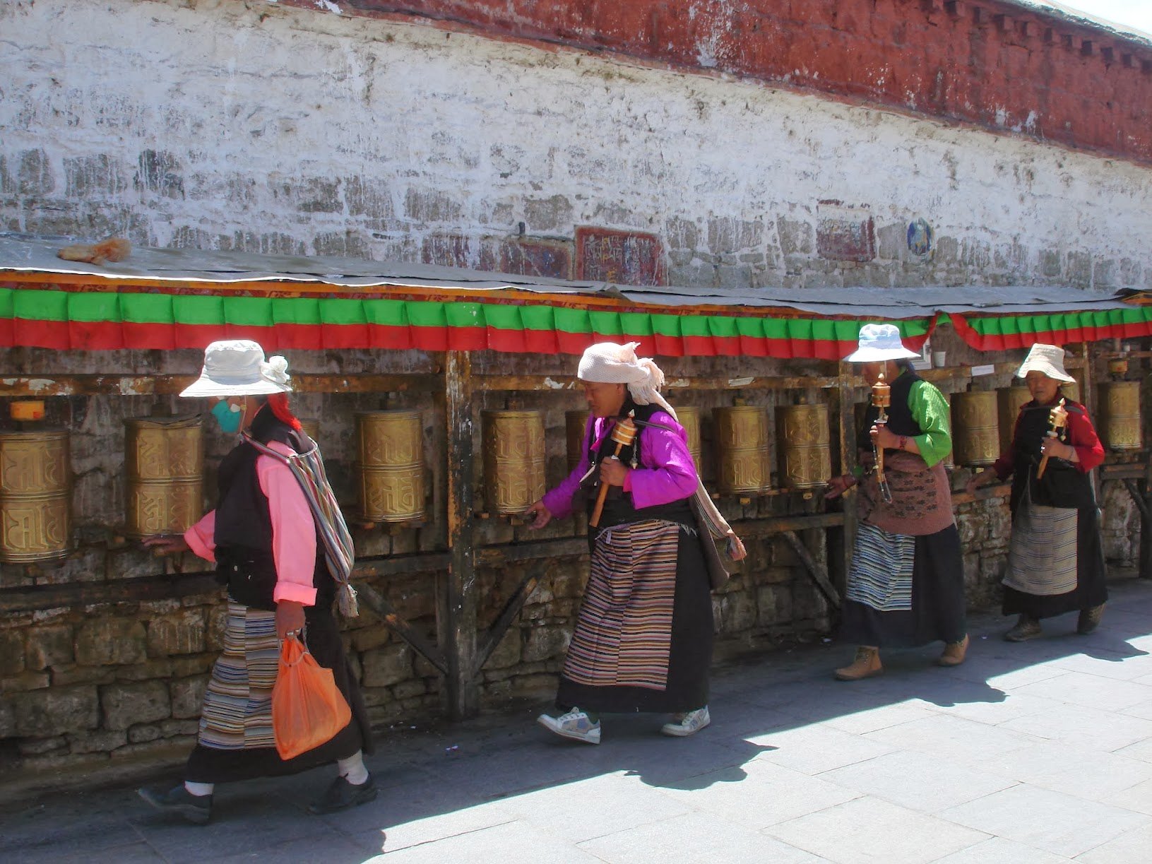 A group of Tibetan women wearing traditional Tibetan clothing and prayer beads, with their hands folded in prayer.