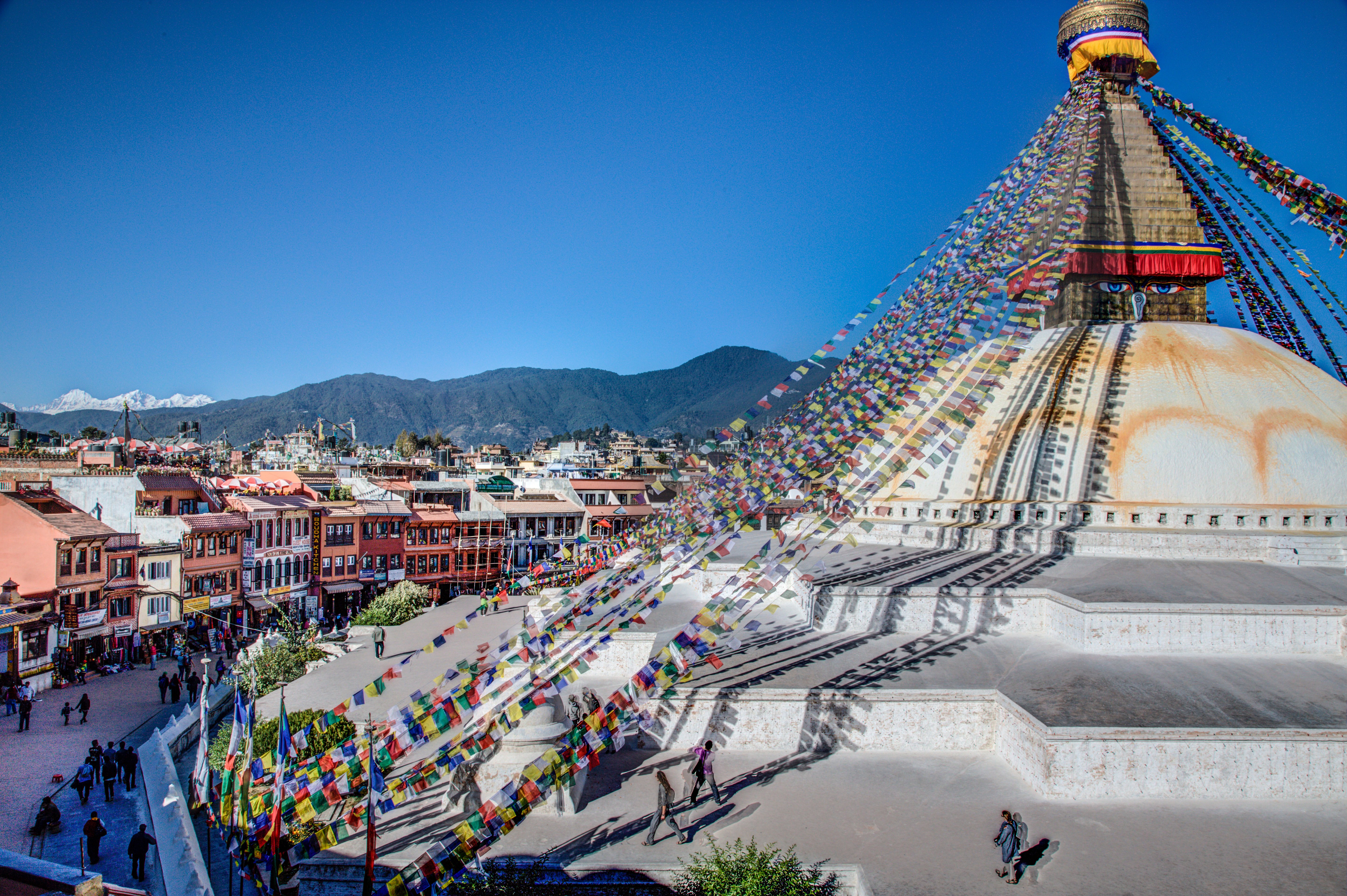  The Boudhanath stupa, a large white dome-shaped structure with a golden spire on top. The stupa is surrounded by colorful prayer flags fluttering in the wind, with traditional Nepalese buildings in the background, painted in bright colours..