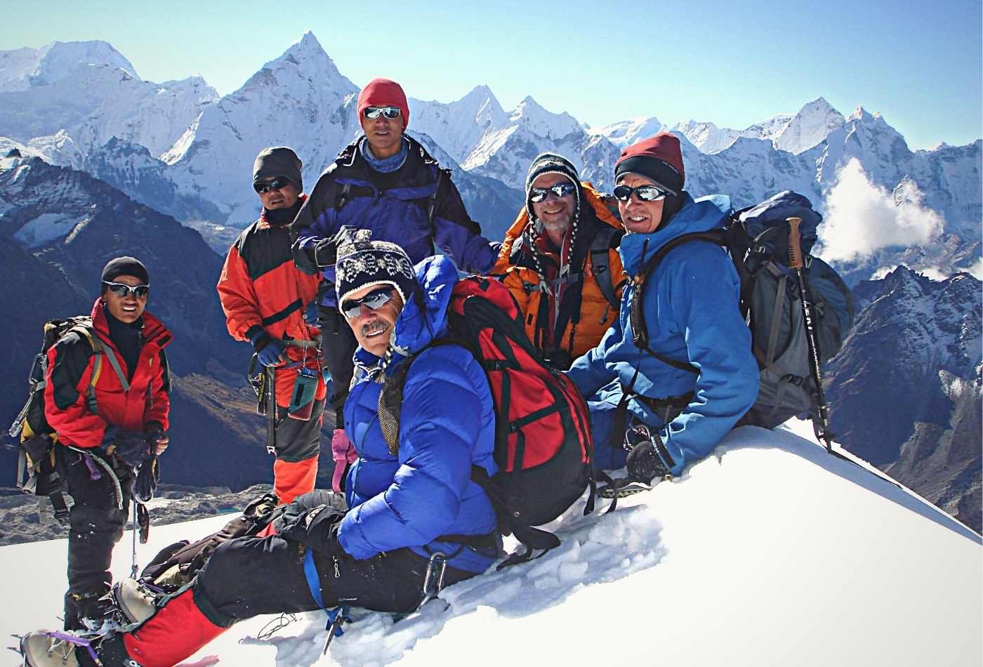 A group of people standing at the summit of Labuche peak, smiling and posing for a photo, with the stunning panoramic view of the Himalayan.