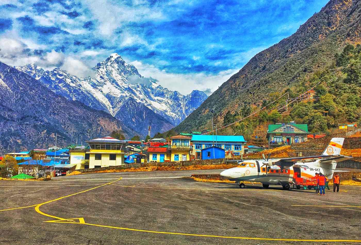 An airplane safely landed on the runway at Lukla Airport, surrounded by houses of Lukla village and with the majestic Kogde mountain looming in the background.