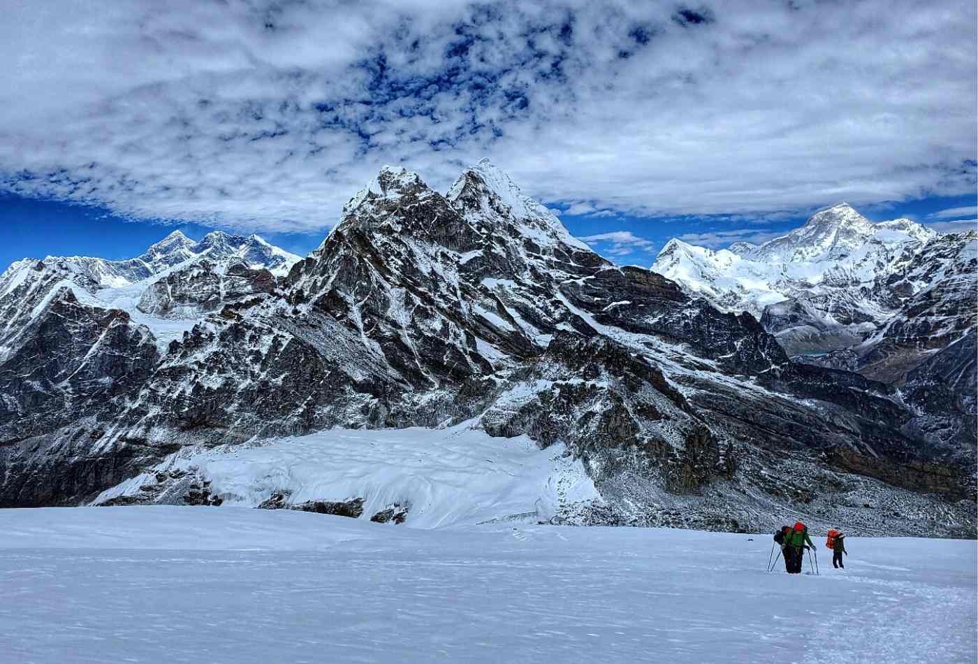 A determined climber making their way up a snowy path towards a high camp, with majestic Mt. Everest and Mt. Makalu towering in the background.