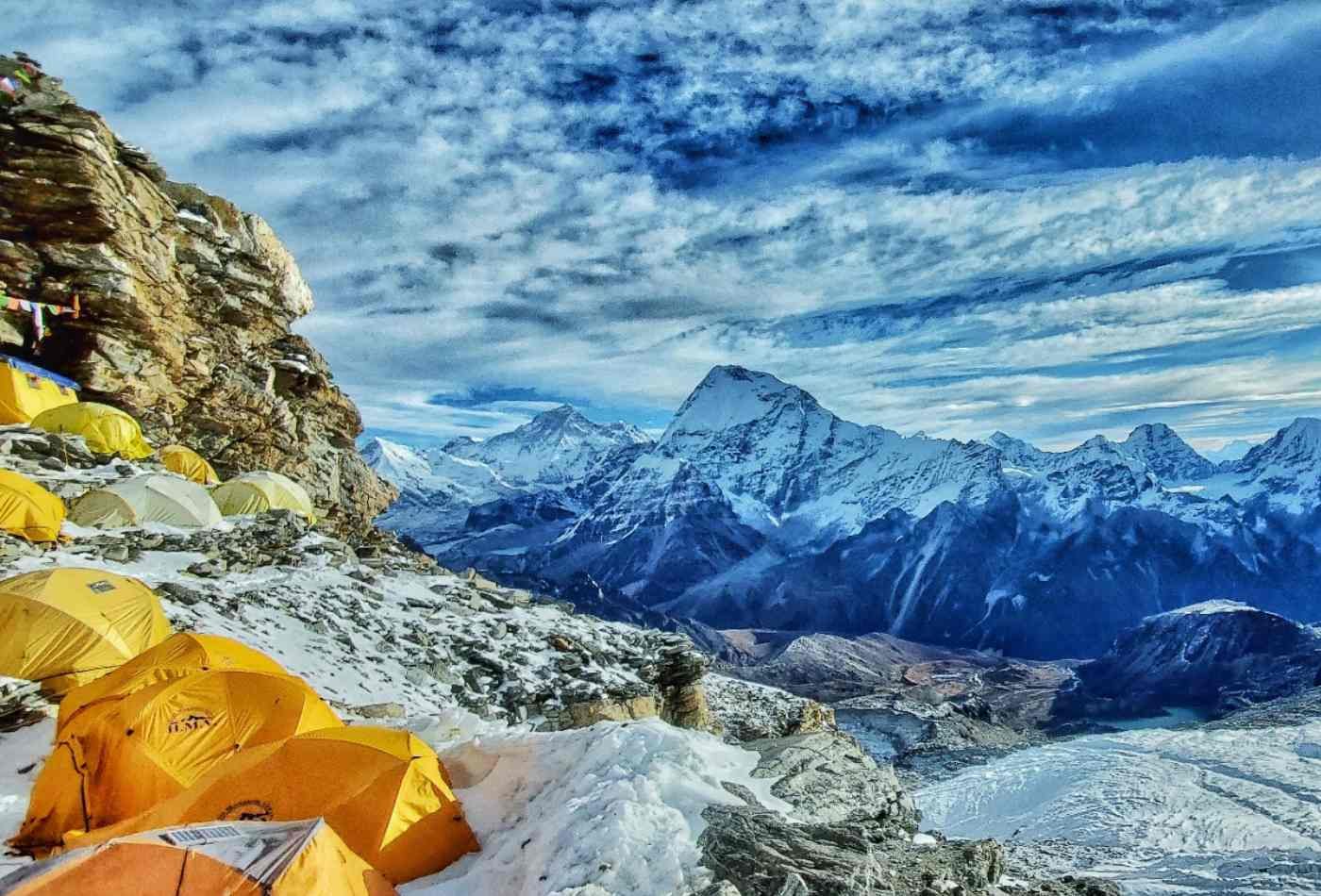 A campsite at Mera High camp with a tent set up on the snowy ground, surrounded by majestic mountains, with white clouds filling the blue sky.
