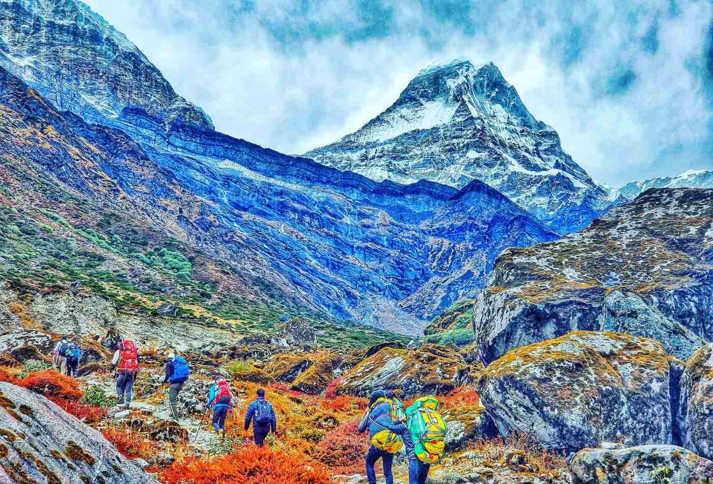 A group of trekkers making their way through the shadow cast by the majestic Kyashar Peak, with the mountain towering in the background.