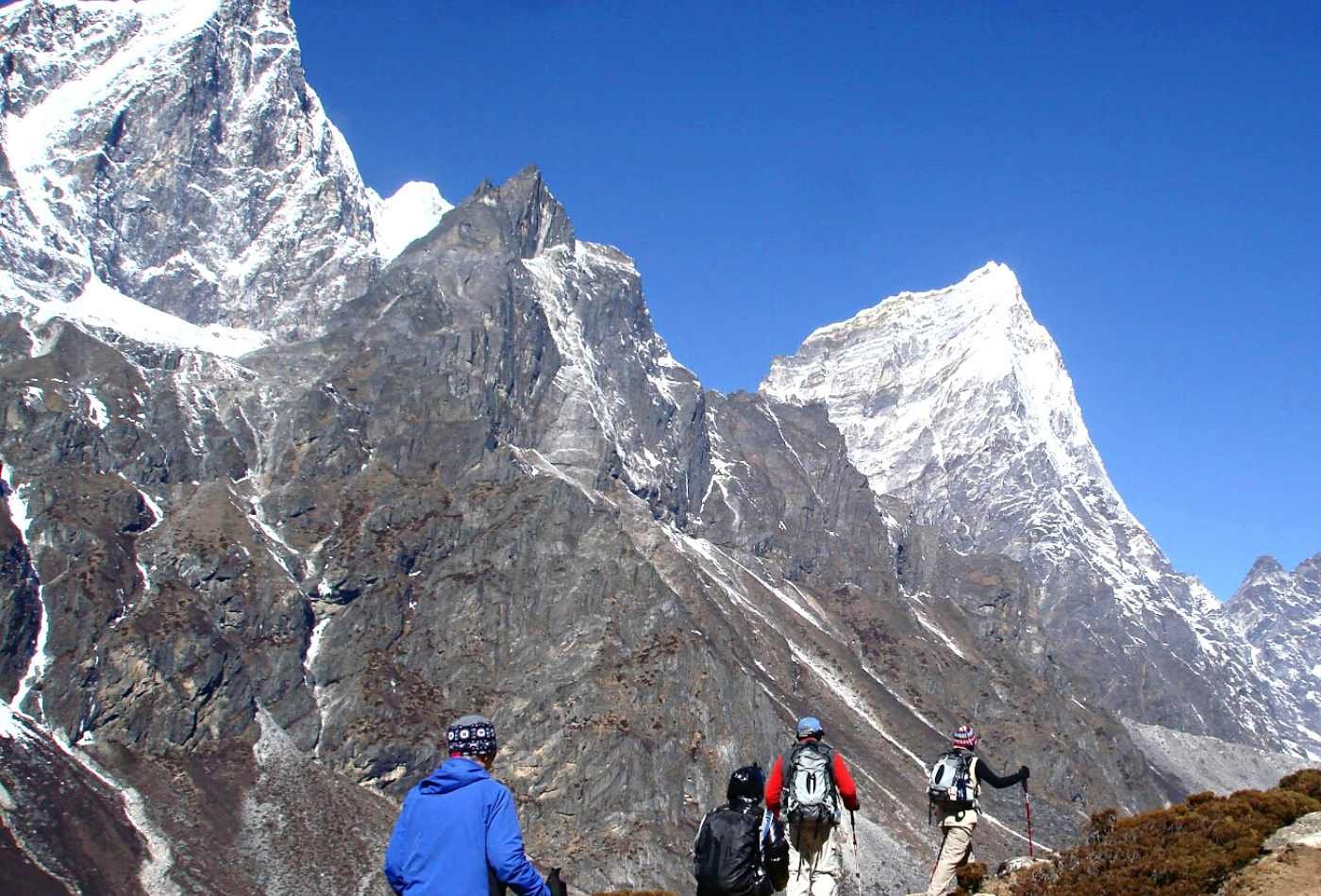 A view of Cholatse Peak during the Everest Base Camp Trek with a group of trekkers walking on a rocky trail surrounded by mountains and snowy peaks. 