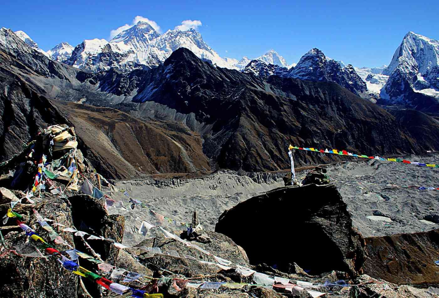 A breathtaking view of Mount Everest from Gokyo-Ri, with prayer flags in the foreground and the mountain surrounded by other majestic peaks.