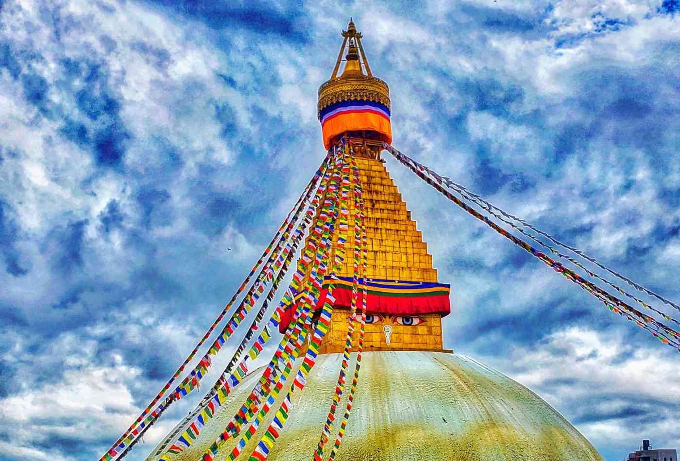 A majestic view of the Bouddhanath Stupa, surrounded by prayer flags fluttering in the wind and the iconic Buddha eyes, gazing down upon the scene.
