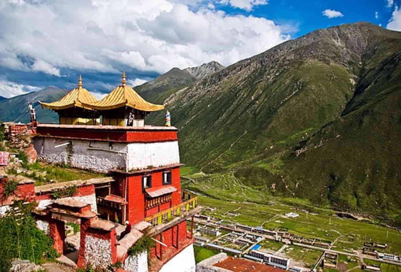 Drigung Till Monastery, with its red painted walls and green hills in the background, stands tall against the clear blue sky.