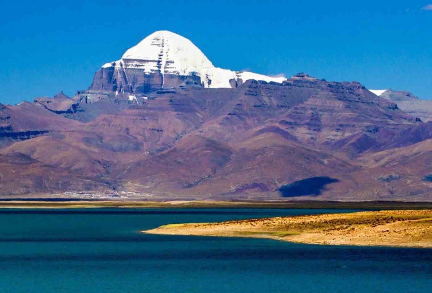 A majestic view of Mt. Kailash, a sacred mountain in Tibet, in a clear sky with a lake in the foreground.