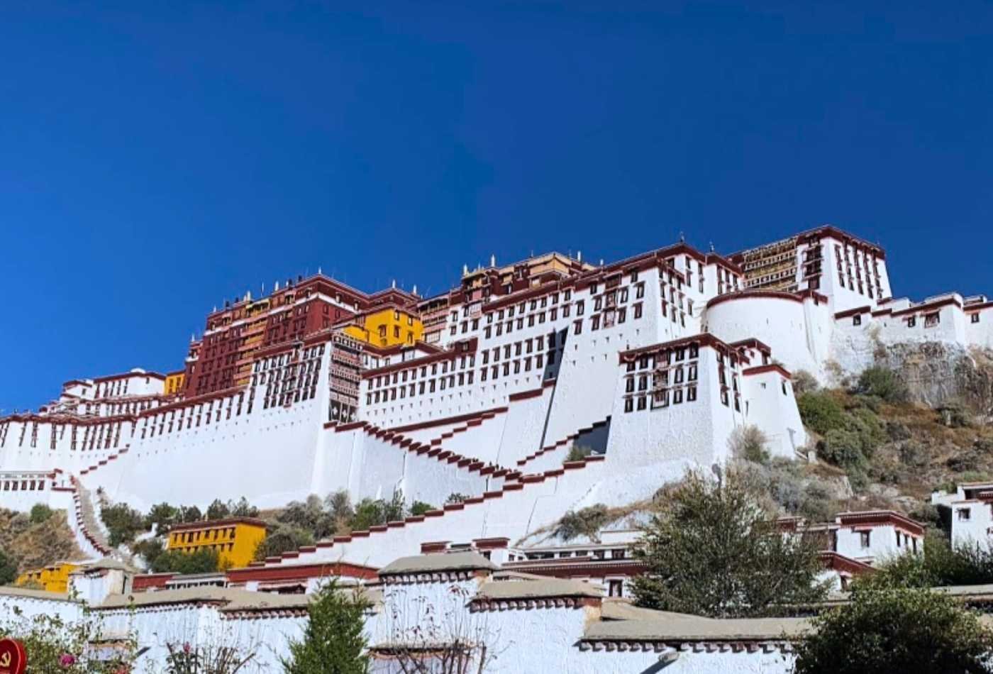 The Potala Palace in Lhasa, Tibet, with its distinctive white and red color scheme and a clear blue sky in the background.