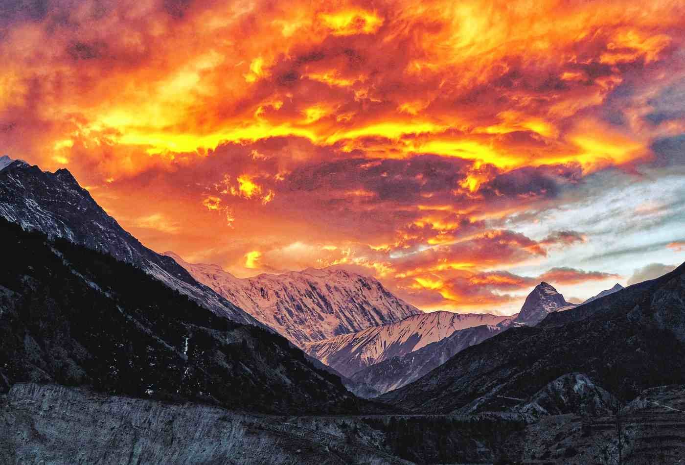 A breathtaking view of Tilicho Peak (7,134m) during sunset with clouds in the sky. The peak stands majestically in the background, with its summit bathed in warm orange and pink hues of the setting sun