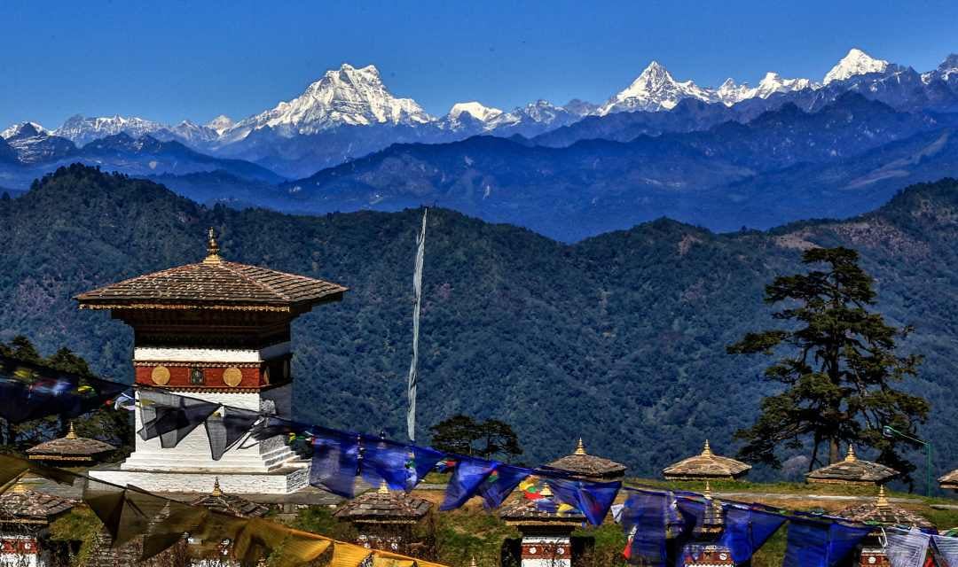 Dochu La Pass, a mountain pass in Bhutan, with a stunning view of snow-capped peaks in the background, and a small monuments in foreground.