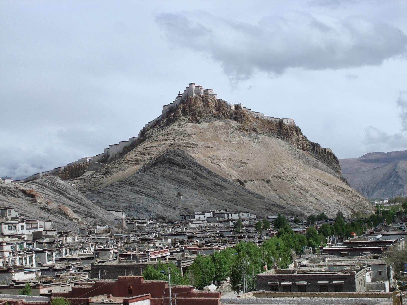 Tibetan small town in between the high hills with green trees in middle. 
