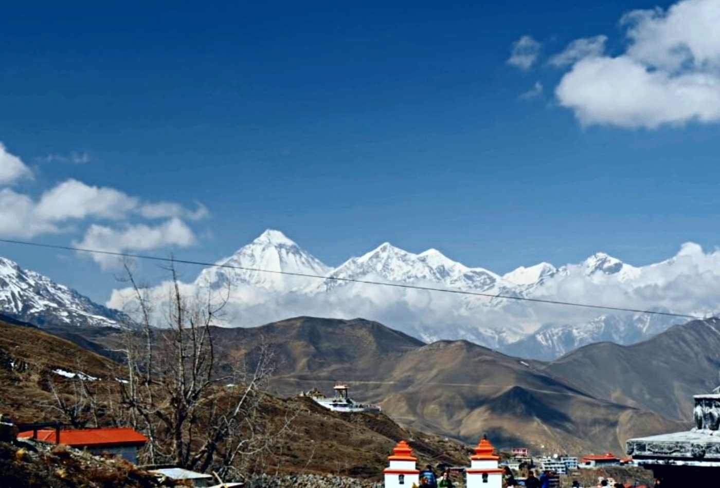 An aerial view of the majestic peaks of Mt. Dhaulagiri and Tukuche with scattered clouds in the sky, captured from the vantage point of Muktinath.