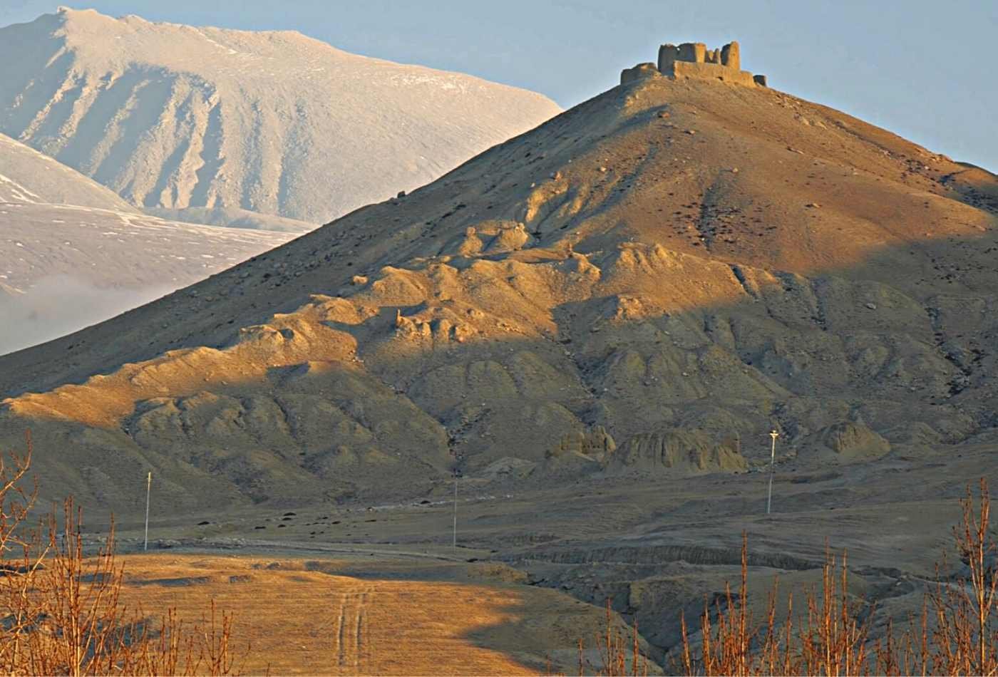 An ancient fortress perched atop a hill, basked in warm sunlight with a barren, arid landscape in the background in Upper Mustang. 