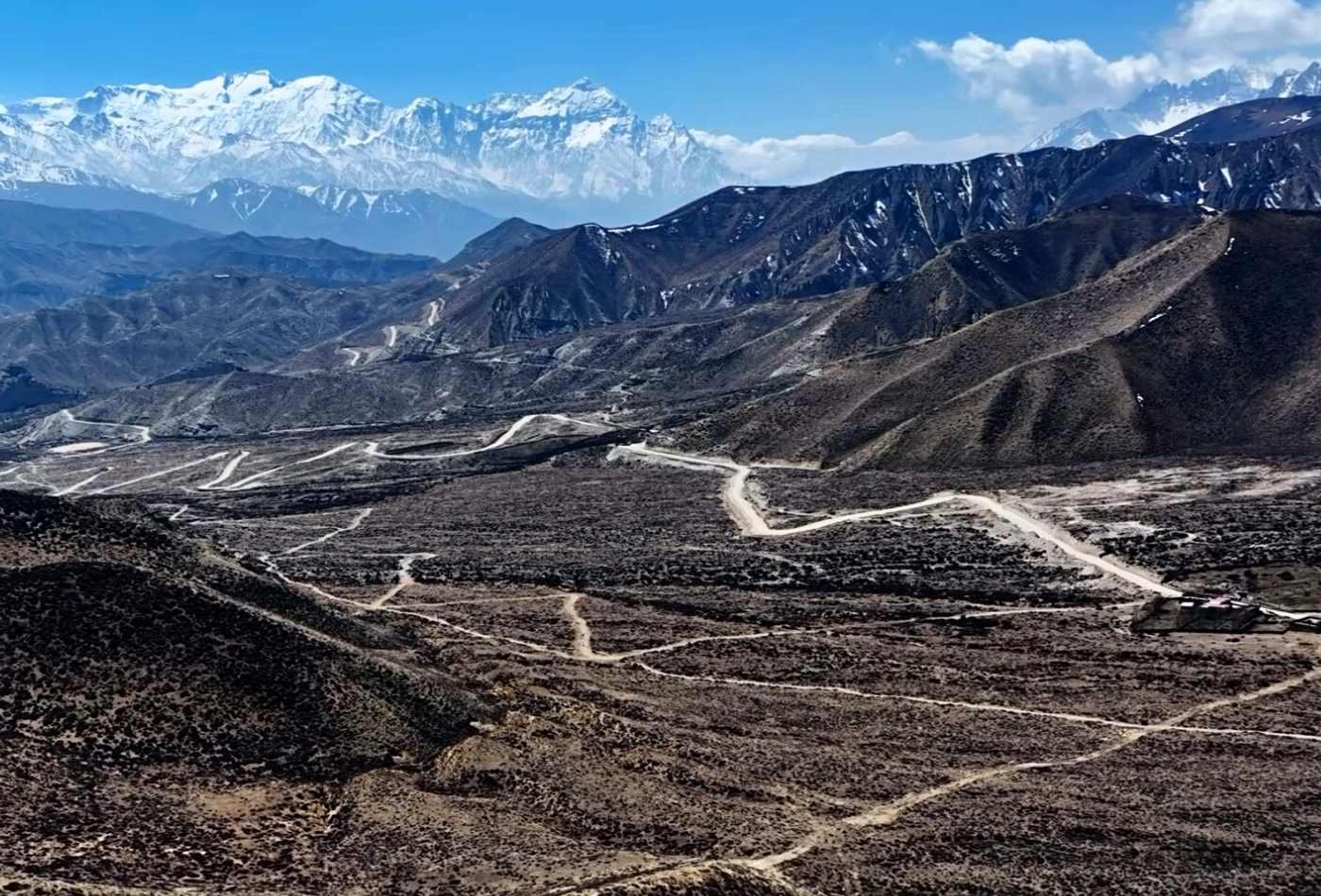 A winding road leading to the town of Lo-Manthang with the majestic Mt. Nilgiri and Tilicho Peak towering in the background.
