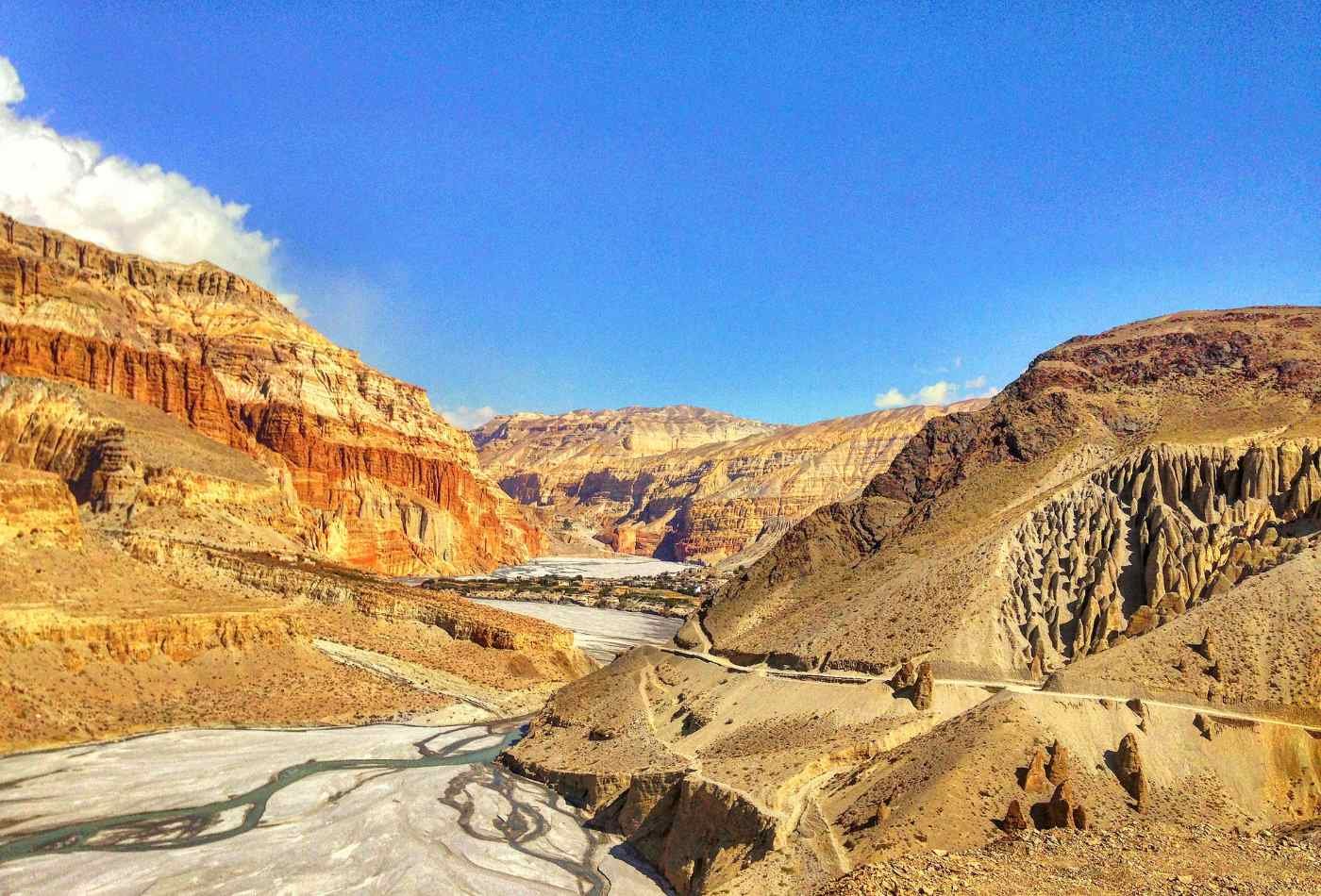 A scenic view of the red and arid hills with the Kali Gandaki River flowing through and a road leading to the remote town of Lo-Mangthang.
